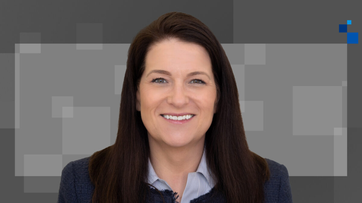 Woman with long brown hair wearing a blue collared shirt and black blazer, set against a gray background with pixelated squares.