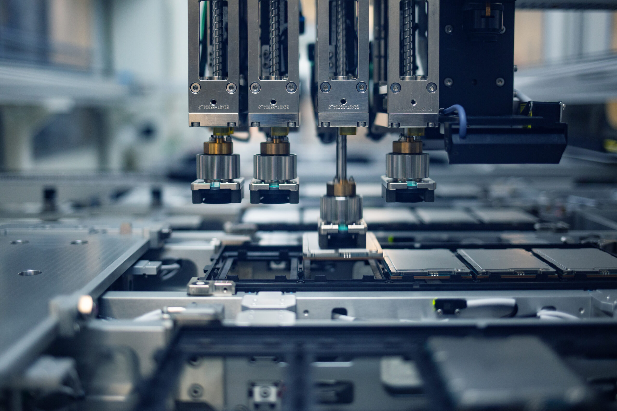 A close-up view of an industrial machine with multiple robotic arms working on an assembly line in a factory setting. The machinery is equipped with various components, indicating high-tech manufacturing or electronics production.