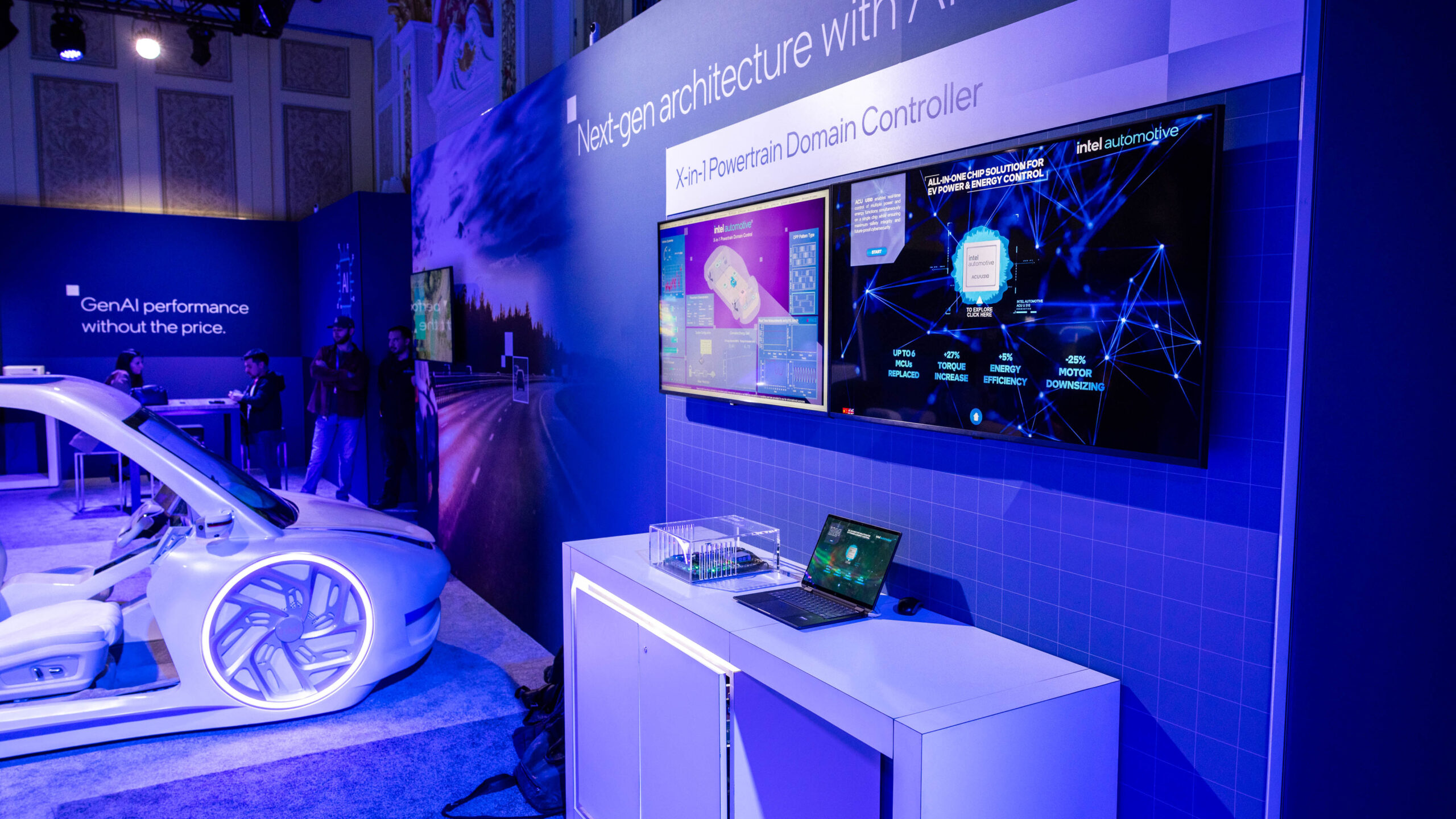 A technology exhibition booth showcasing automotive innovations. The setup includes a futuristic car model, digital displays with graphics about car architecture, a laptop, and signage about AI performance. The lighting is bright and modern.