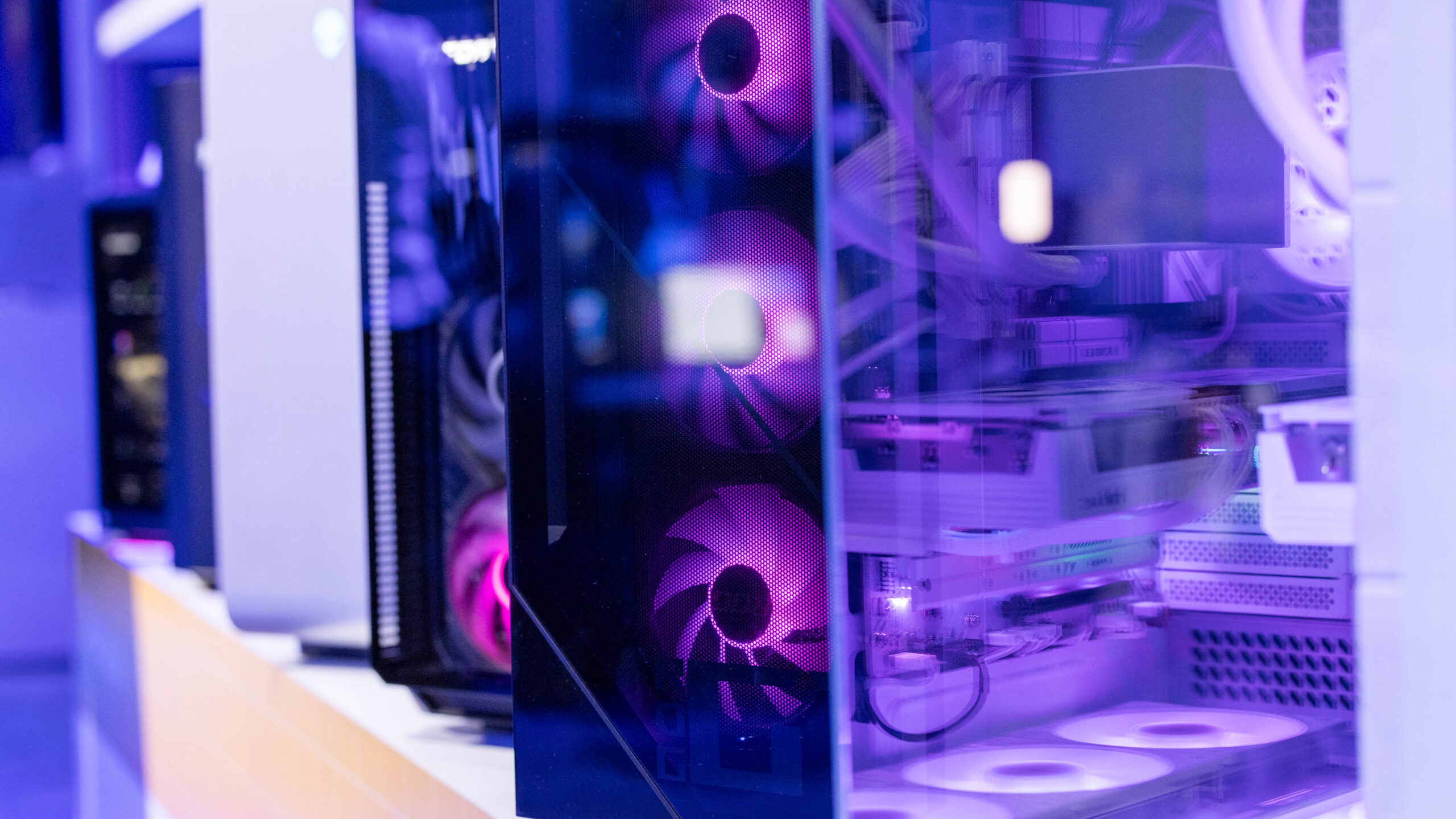 A close-up view of a modern gaming PC with purple LED lighting. The transparent case showcases internal components, including fans and cables, under ambient lighting.
