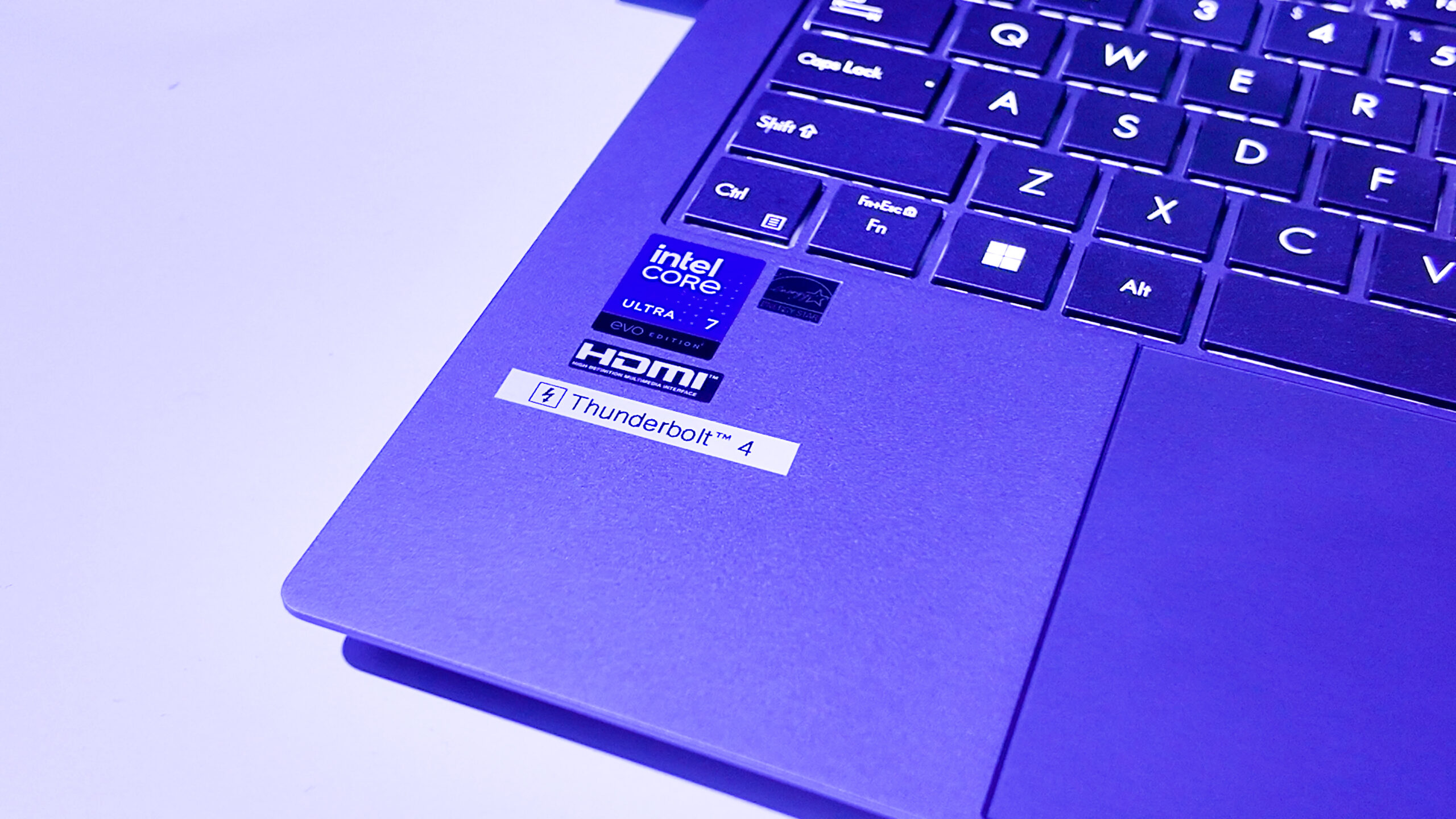 Close-up of a purple laptop keyboard and corner. Visible stickers show Intel Core i7, AMD Radeon, HDMI, and Thunderbolt 4. The keyboard features black keys and a power button.