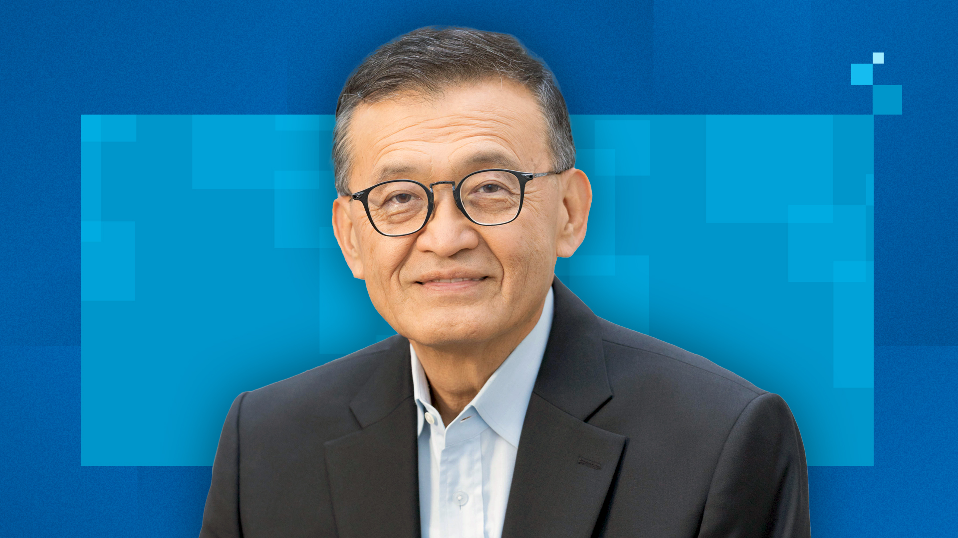 An older adult with short hair wearing glasses and a dark suit jacket against a blue geometric background.