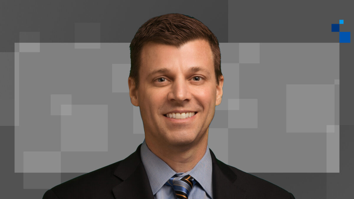 Man in a suit and tie smiling against a pixelated gray background.