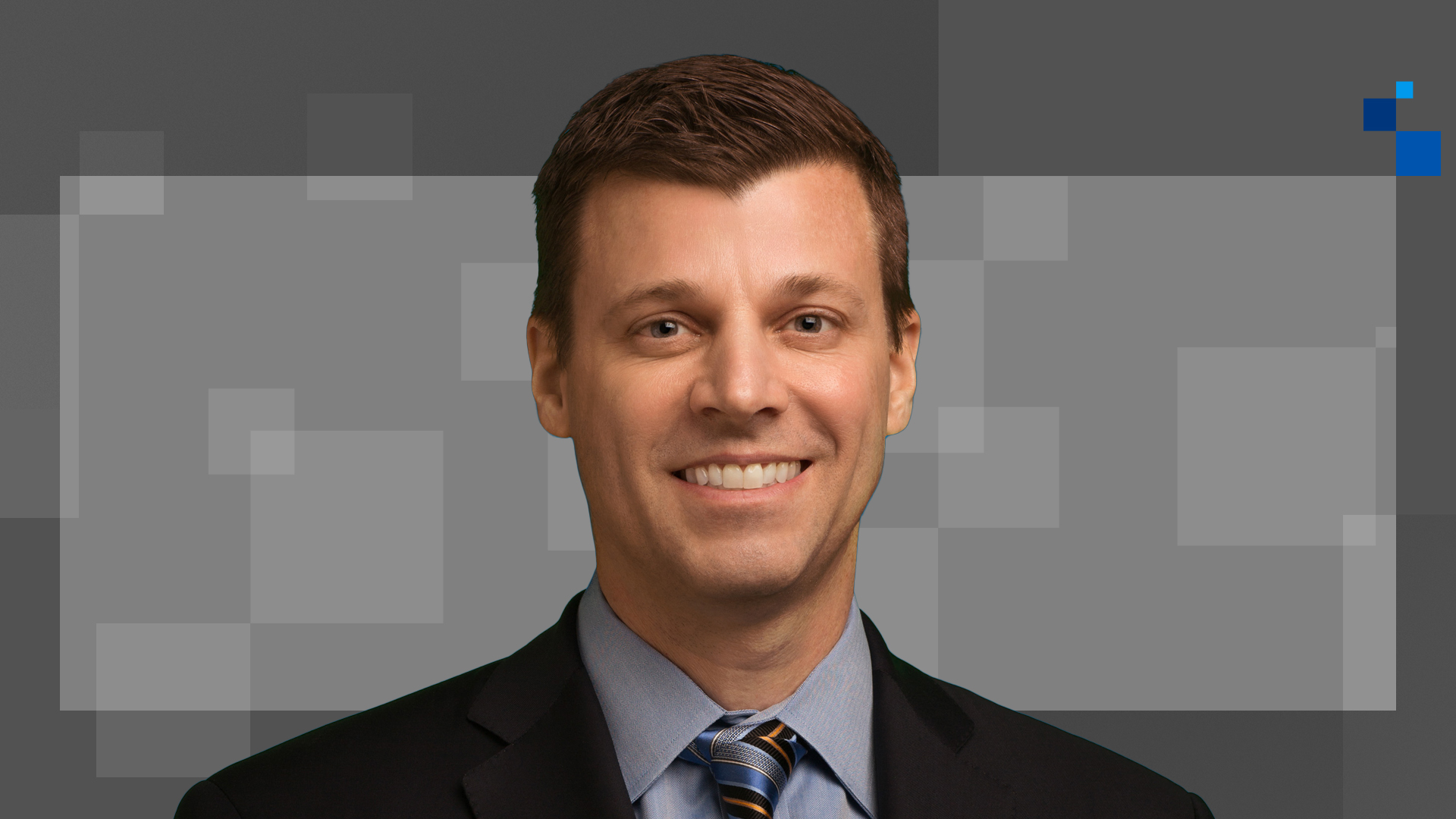 Man in a suit and tie smiling against a pixelated gray background.
